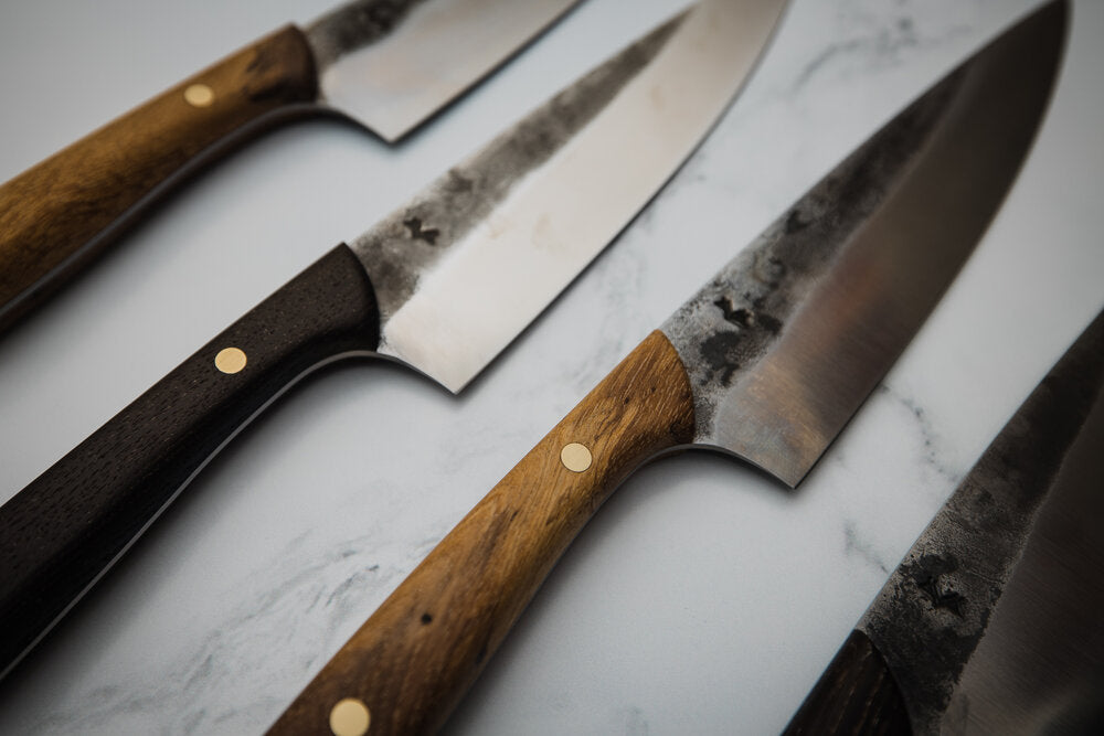 A series of hand forged chef knives on a marble counter