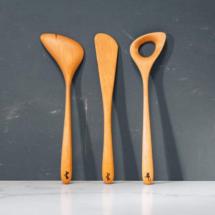 Two wooden spoons and a wooden spatula with a dark gray background.