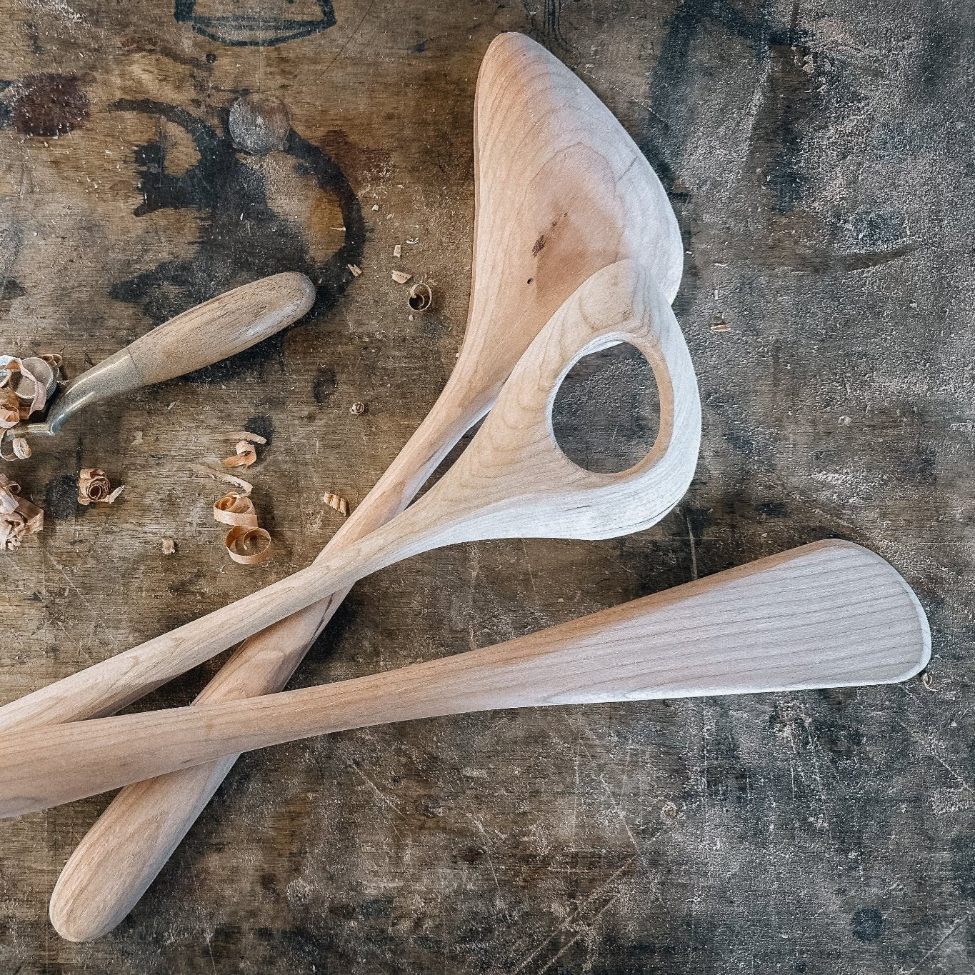 Unfinished wooden cooking utensils on a rustic workbench background.