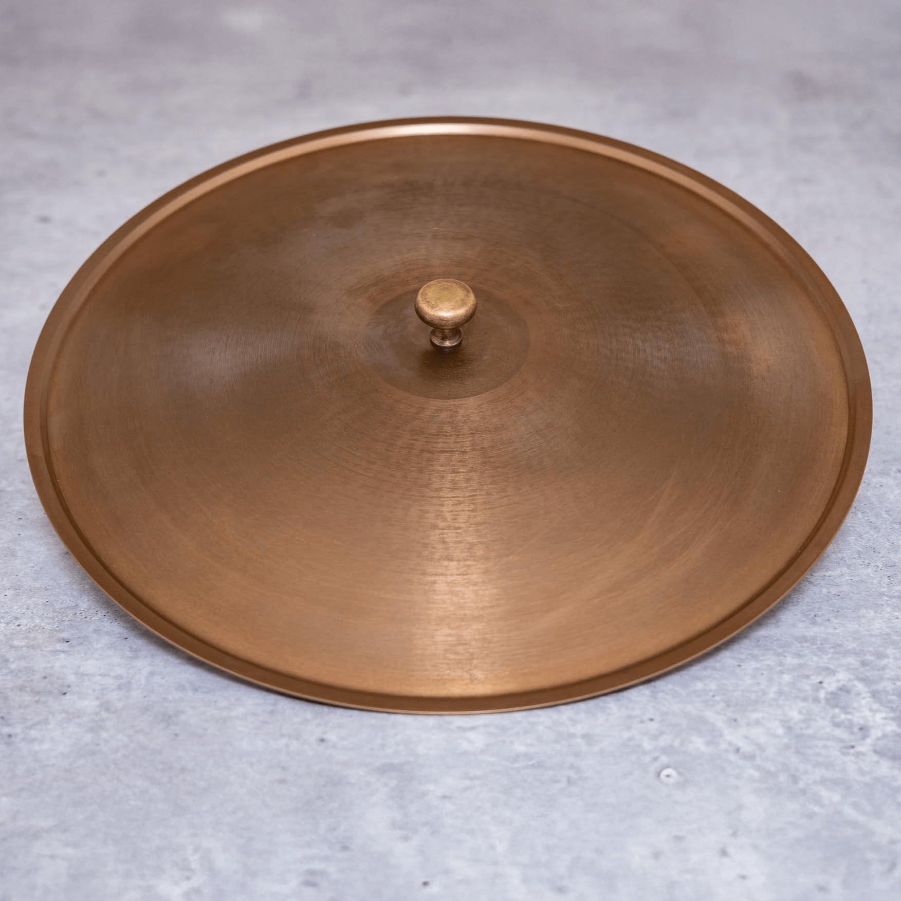 A bronze-colored stainless steel lid with a central knob, placed on a grey surface.