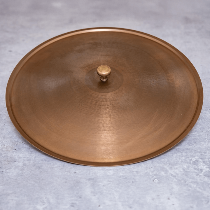 A bronze-colored stainless steel lid with a central knob, placed on a grey surface.