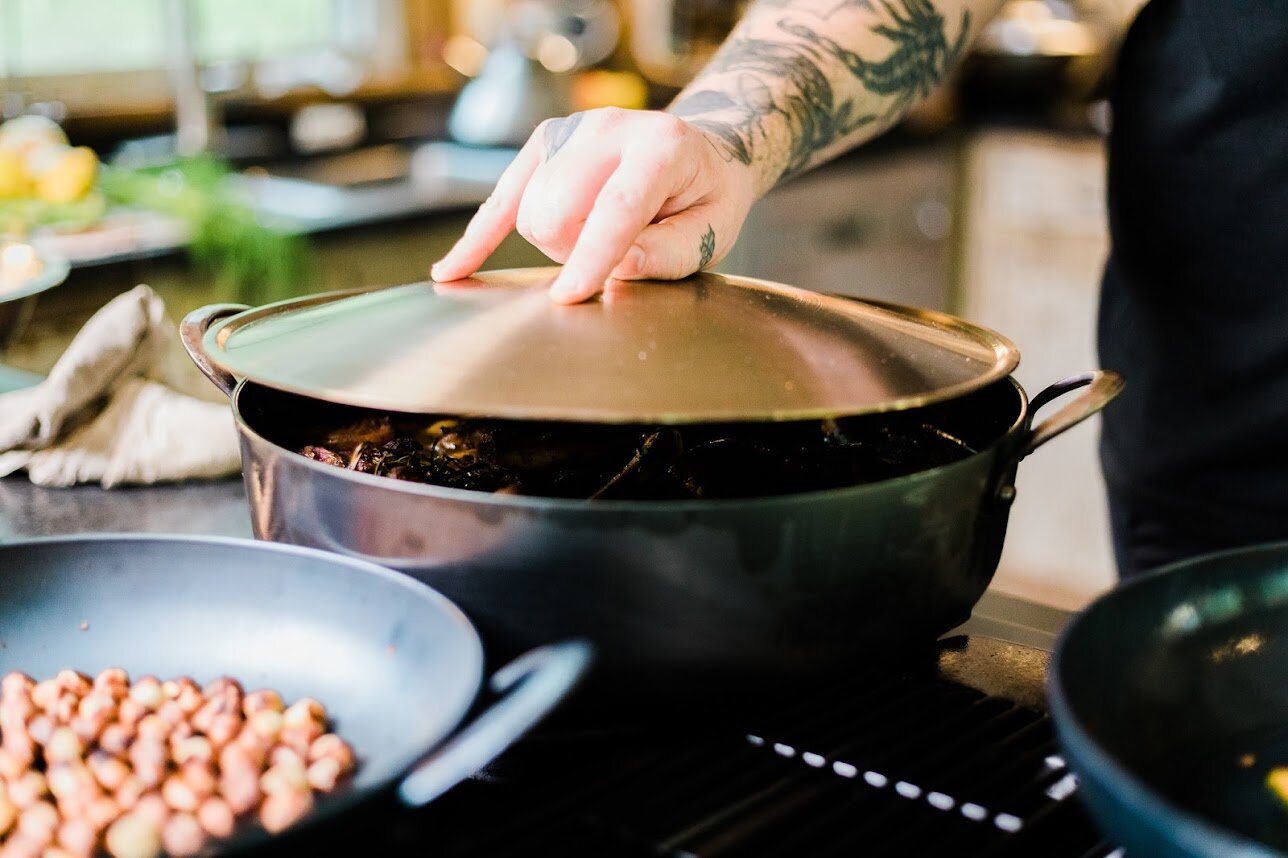 A chef cooking on a gas stove with a hand forged carbon steel pro rondeau with bronze handles and stainless steel lid set