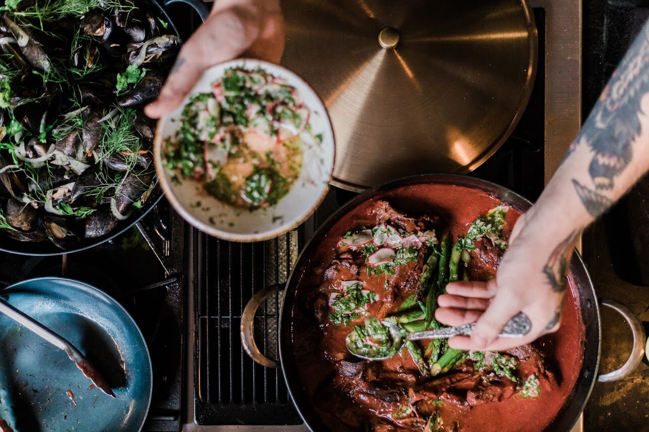 Chef spooning vegetables out of a handcrafted carbon steel pro rondeau on a gas stove