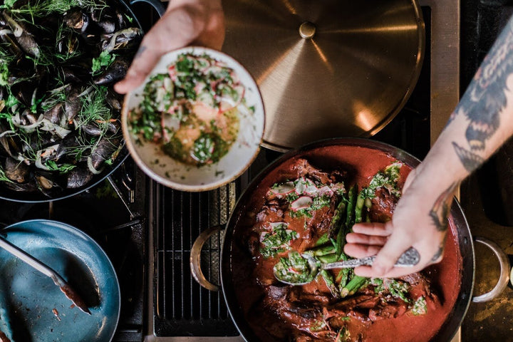 Chef spooning vegetables out of a handcrafted carbon steel pro rondeau on a gas stove