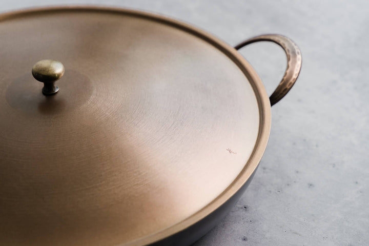 Handcrafted carbon steel saucier with bronze handles and stainless steel lid