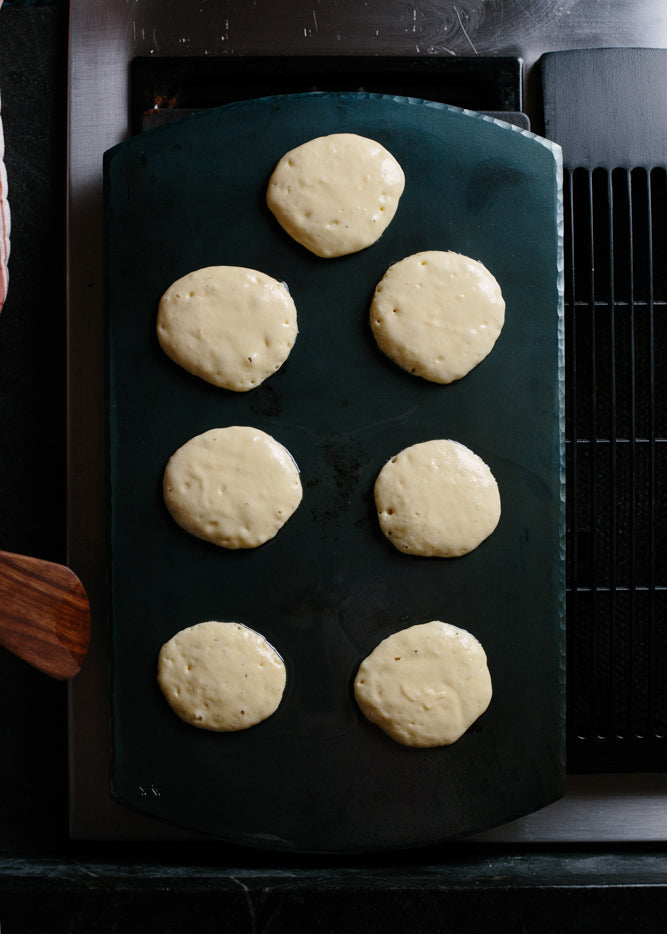 A handmade, handcrafted carbon steel bakeware sheet on top of an oven with pancakes baking on top