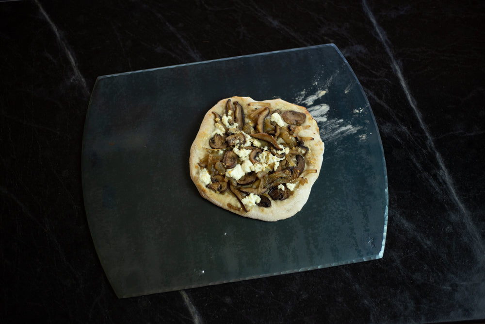 A handcrafted carbon steel steel bakeware sheet with a handmade pizza resting on top