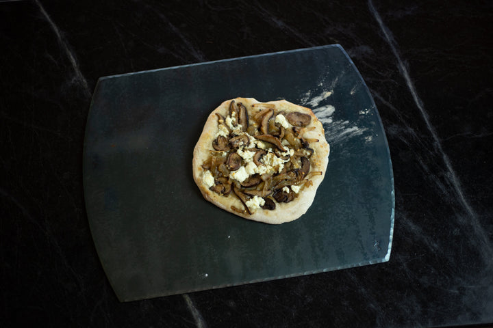 A handcrafted carbon steel steel bakeware sheet with a handmade pizza resting on top