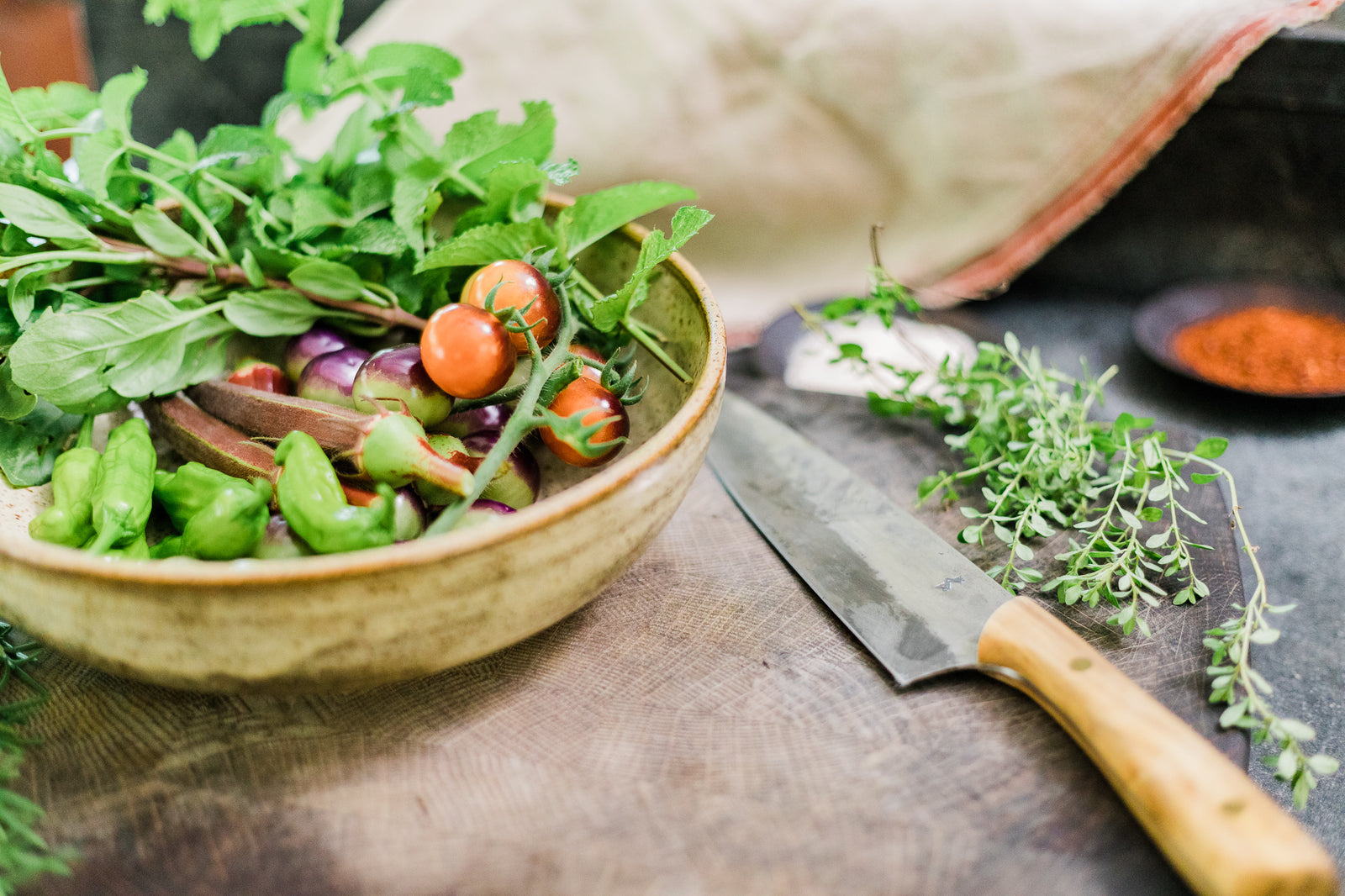 Handmade ceramic bowl of vegetables with a hand forged knife aside it
