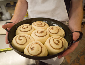 Baker holding raw, uncooked cinnamon rolls in a carbon steel saucier pan