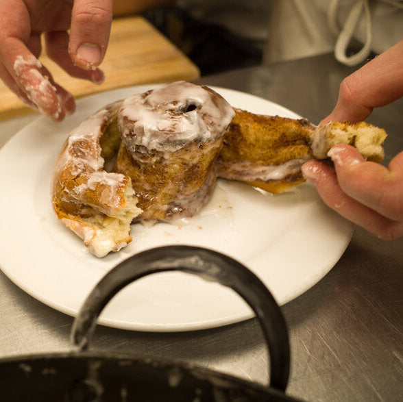 Hands pulling apart a cinnamon roll on a plate