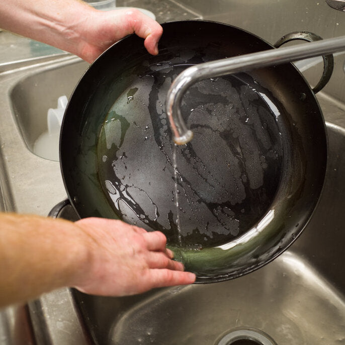 Baker washing a carbon steel saucier in an industrial kitchen sink