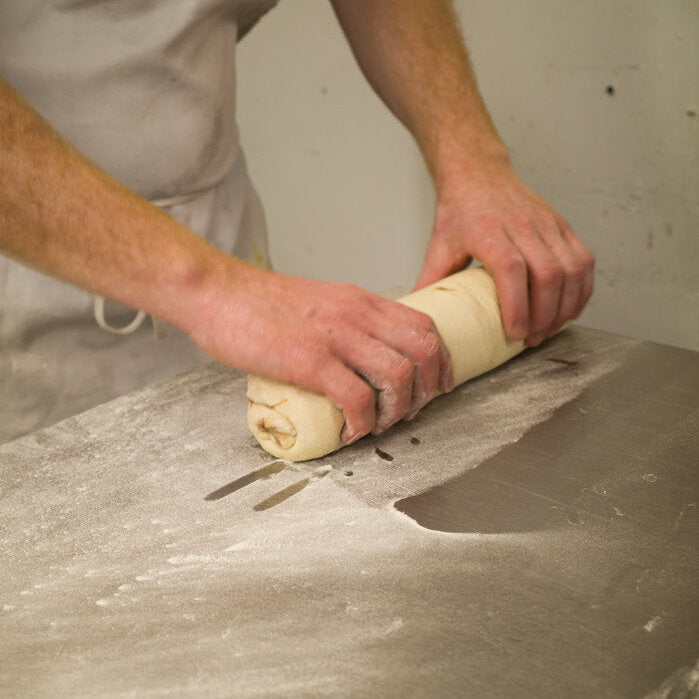 Baker rolling up dough for cinnamon rolls