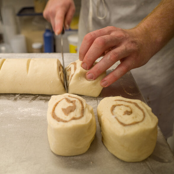 Baker slicing cinnamon roll dough into pieces 