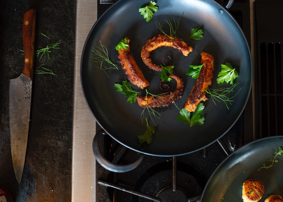 Hand forged, artisan eleven inch carbon steel pro roaster on a stove with herbs and scallops