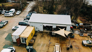 Fly over shot of a blacksmithing garage, two shipping containers and many cars