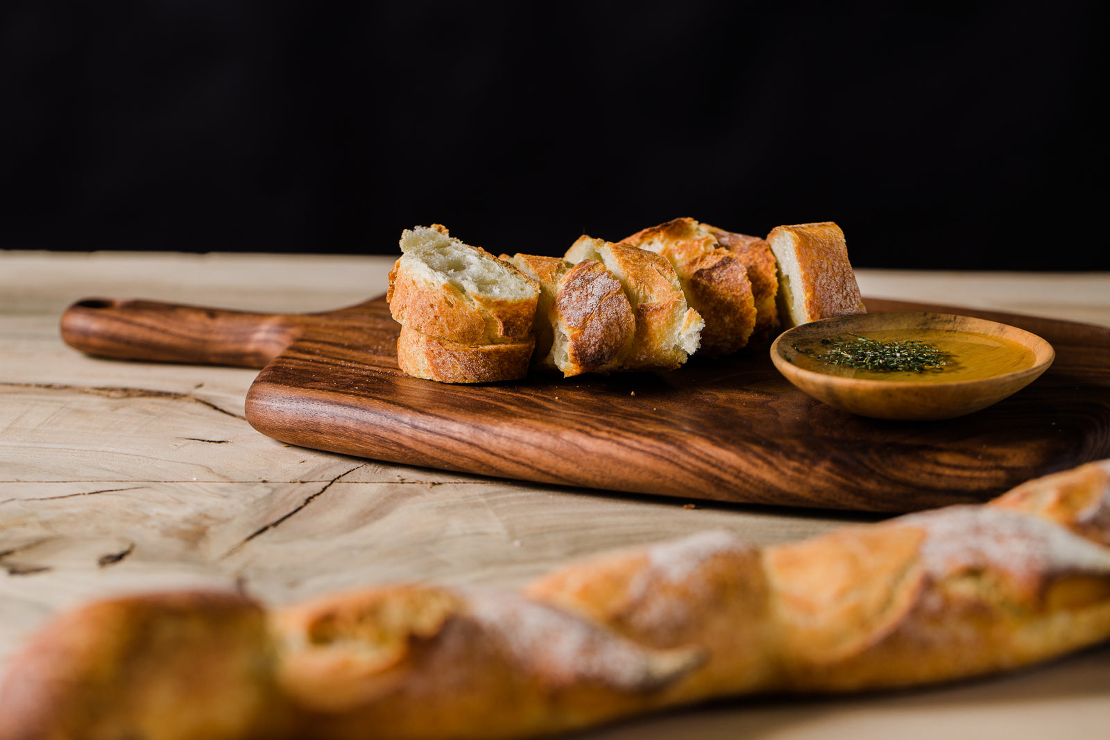 Handmade wooden serving board with sliced bread and a pinch bowl of olive oil on top