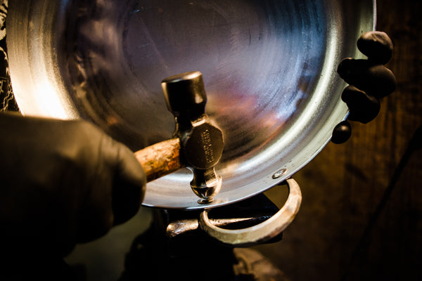 Artisan hammering the handle onto a carbon steel pan base 