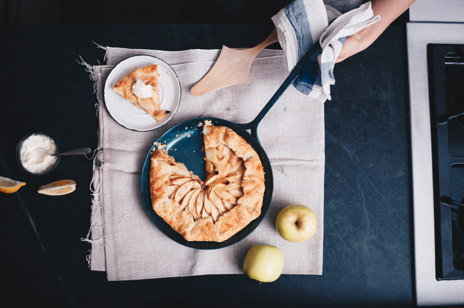 Rustic apple galette missing a slice in a carbon steel skillet pan lying on a linen napkin with whole apples and a plate with the missing slice on it