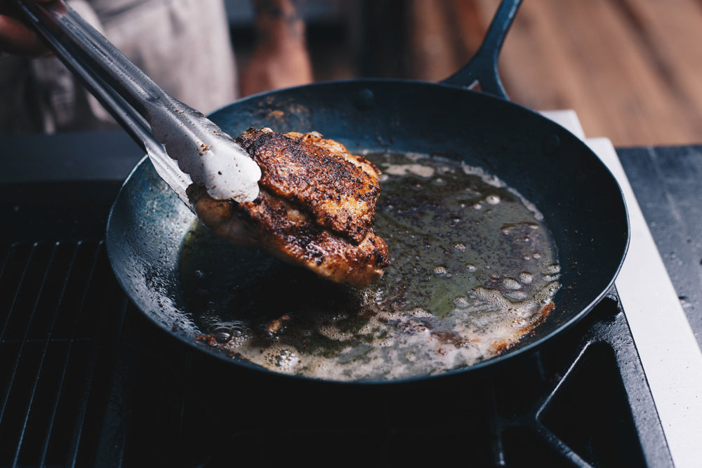 Handcrafted heritage skillet with a piece of chicken being roasted in oil on it