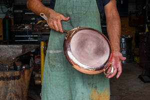 Blacksmith holding a copper skillet pan standing in a workshop