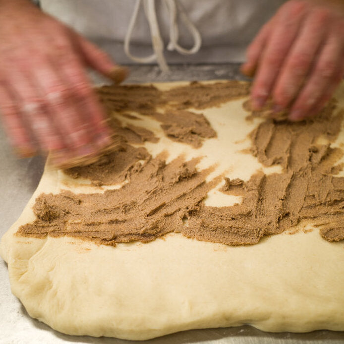 Dough being rubbed with cinnamon sugar by baker