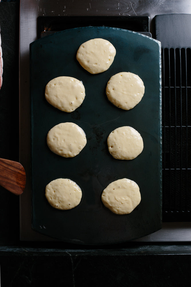 A handmade, handcrafted carbon steel bakeware sheet on top of an oven with pancakes baking on top 