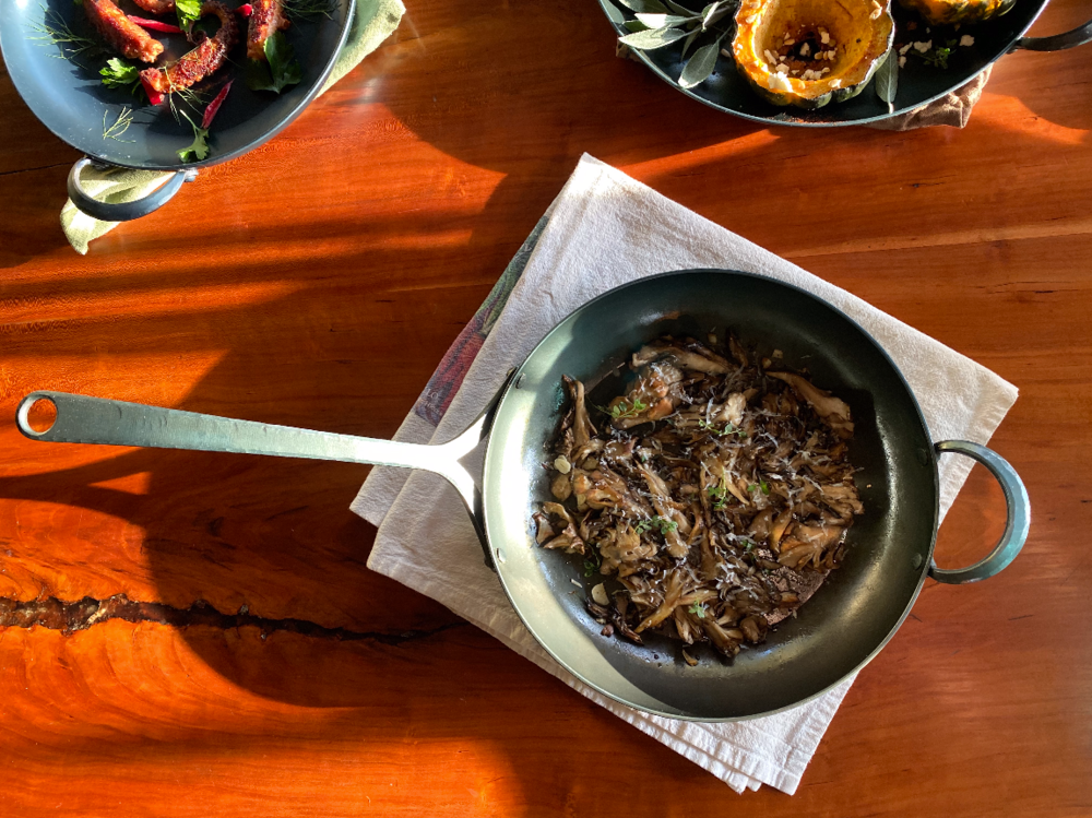 A downward shot looking at a handmade eleven inch carbon steel pan filled with roasted mushrooms on top of a linen napkin