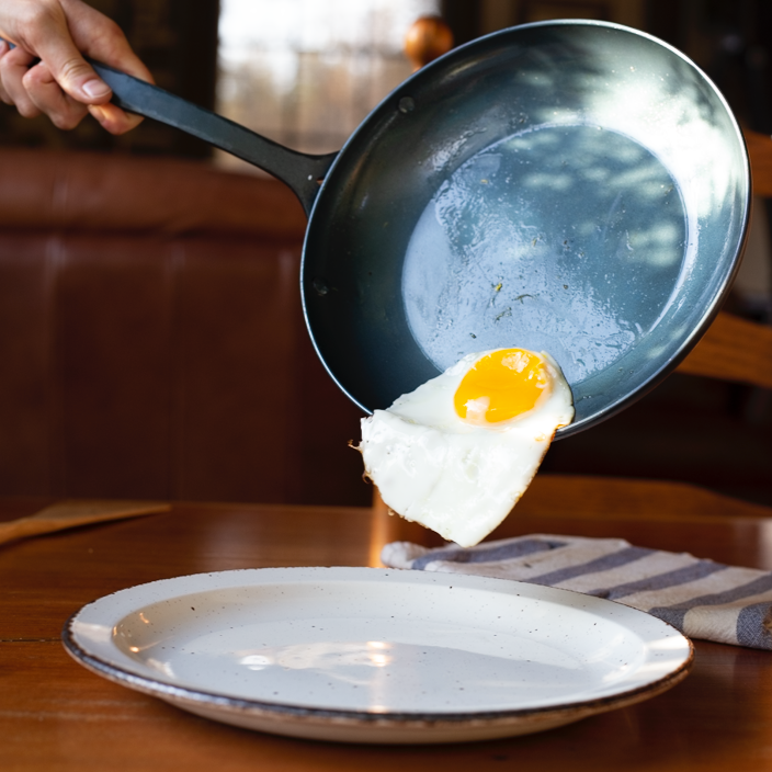 Handcrafted carbon steel pan with a fried egg sliding off it onto a plate below 