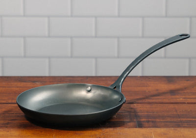 A handcrafted, hand forged nine inch pro carbon steel skillet on a wooden table 