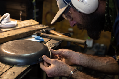 Man forging carbon steel pan in a shop wearing work glasses and protective ear wear